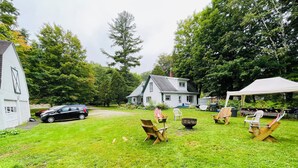 Une cour verdoyante avec une maison blanche, une tente et plusieurs chaises en bois.