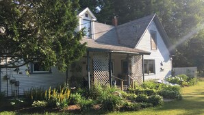 Une maison avec un porche, un petit garage attenant et un jardin agrémenté de diverses plantes et fleurs.