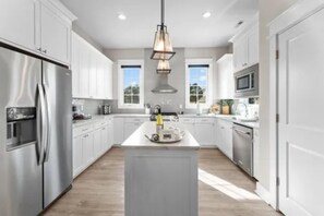 Une cuisine moderne avec des meubles blancs, des appareils en acier inoxydable et un îlot central.