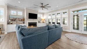 A modern living room with a grey sectional sofa, a fireplace, a flat-screen TV, and a ceiling fan. - Charming 3 bedroom beach house in Cape Charles, VA  (Cape charles)