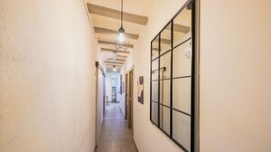 A narrow hallway with a tiled floor, a large window with a grid pattern, and a hanging light fixture.