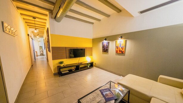 A modern living room with a sofa, a coffee table, and a TV on a stand. There is a hallway leading to another room.
