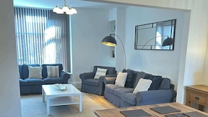 A modern living room with a wooden dining table, two sofas, a white coffee table, and a floor lamp. - Beautiful 4BR Home near Chester Racecourse (Chester)