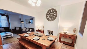 A dining area with a wooden table set for four, benches, a wall clock, and a small side table with a lamp. - Beautiful 4BR Home near Chester Racecourse (Chester)