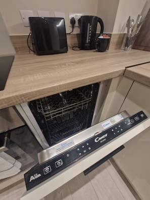 A kitchen with a dishwasher, a coffee maker, and a set of utensils on the counter. - Elegant 1Bed Apt in Leeds City Centre (Leeds)