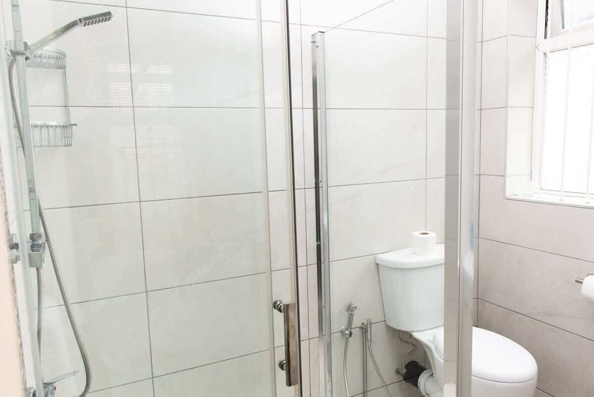 Eine Duschkabine mit Glaswänden, einer Handbrause, einer Toilette und einem Fenster.
