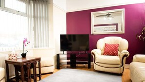 Una sala de estar con televisor, sofá, sillón, una mesita y una ventana con persianas.