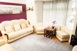 Una sala de estar con un sofá color beige, una mesita de madera y una ventana con persianas.