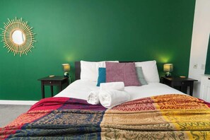 A bed with a colorful blanket, pillows, and a wall-mounted mirror.