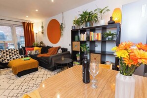 A modern living room with a sofa, ottoman, coffee table, bookshelf, and potted plants. - Modern Retreat: 2BR Apt with Lush Greenery (Sheffield)