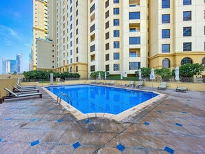 A rooftop pool with lounge chairs and umbrellas, surrounded by a high-rise building with balconies. - Enjoy JBR Sea & Dubai Eye & Marina View (Dubai)