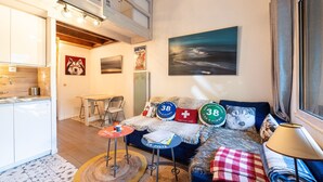 A cozy living room with a sofa, a dining table, a kitchen area, and a painting on the wall. - Apartment 18 with Mountain Views, Private Terrace, and Wi-Fi (Les Allues)