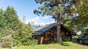 A rustic cabin with a sloped roof, surrounded by dense forest and mountains in the background. - Apartment 18 with Mountain Views, Private Terrace, and Wi-Fi (Les Allues)