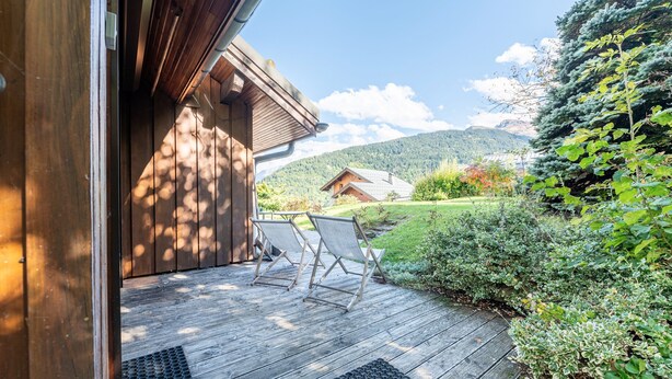 A wooden deck with two chairs, a wooden building, and a mountainous landscape. - Apartment 18 with Mountain Views, Private Terrace, and Wi-Fi (Les Allues)