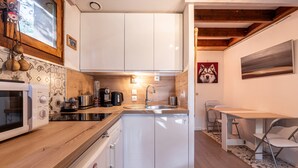 A compact kitchen with white cabinets, a microwave, a sink, and a dining area with a table and chairs. - Apartment 18 with Mountain Views, Private Terrace, and Wi-Fi (Les Allues)