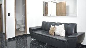 A black leather sofa with two pillows, a wooden door, and a white toilet visible through an open doorway. - HOTEL SANTO RIO SUITE (Santa Marta)