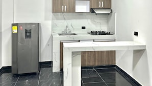 A modern kitchen with a marble countertop, wooden cabinets, a stainless steel refrigerator, and a gas stove. - HOTEL SANTO RIO SUITE (Santa Marta)