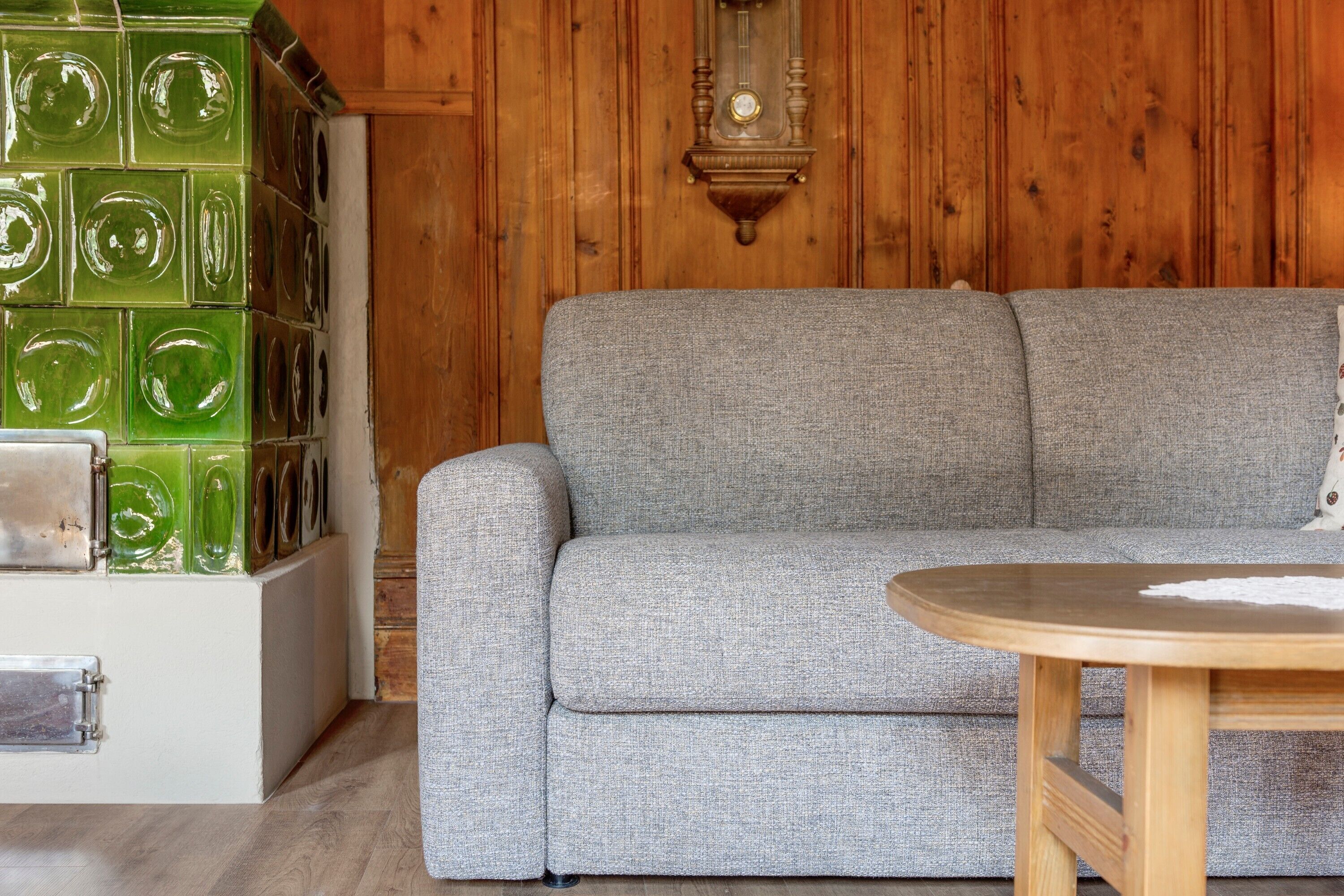 Una habitación con un sofá gris, una mesa de madera y una pared con azulejos de vidrio verde.