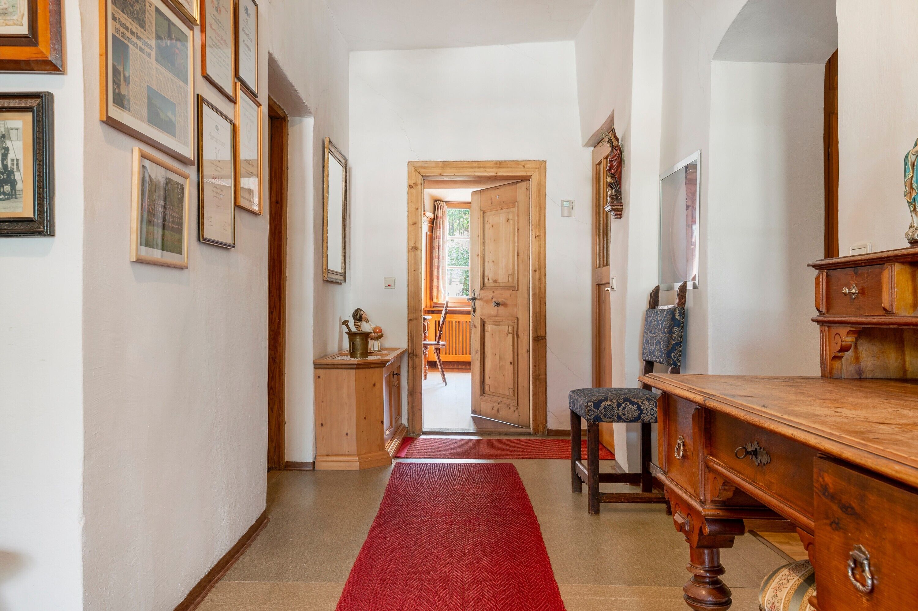 Un couloir orné de tableaux encadrés, un bureau en bois, une chaise et une moquette rouge.
