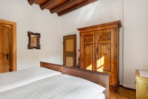 Un dormitorio con un armario de madera, una cama con colcha estampada y una puerta de madera.