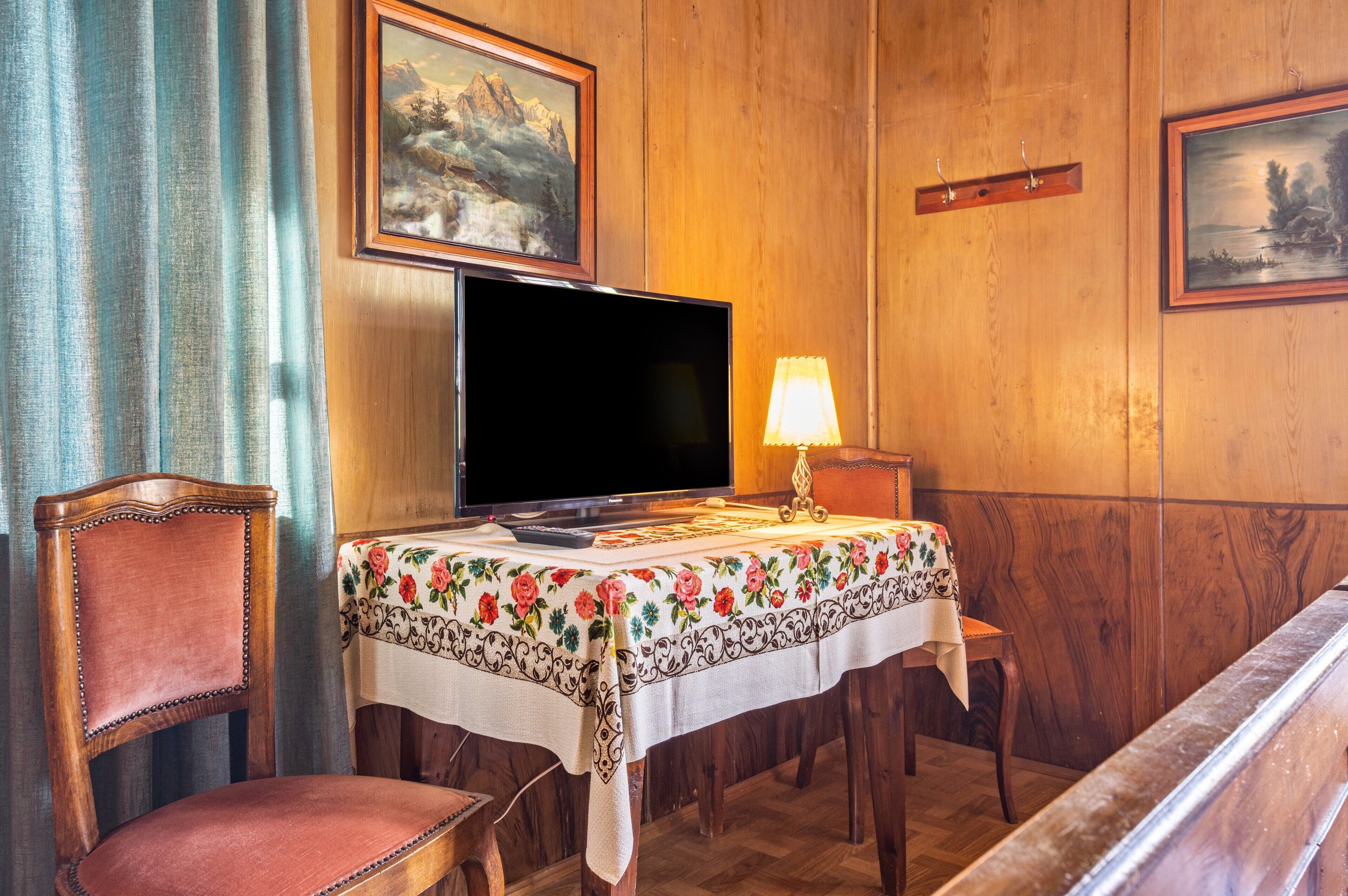 A wooden-paneled room with a television, a table with a floral tablecloth, a chair, and a bench.
