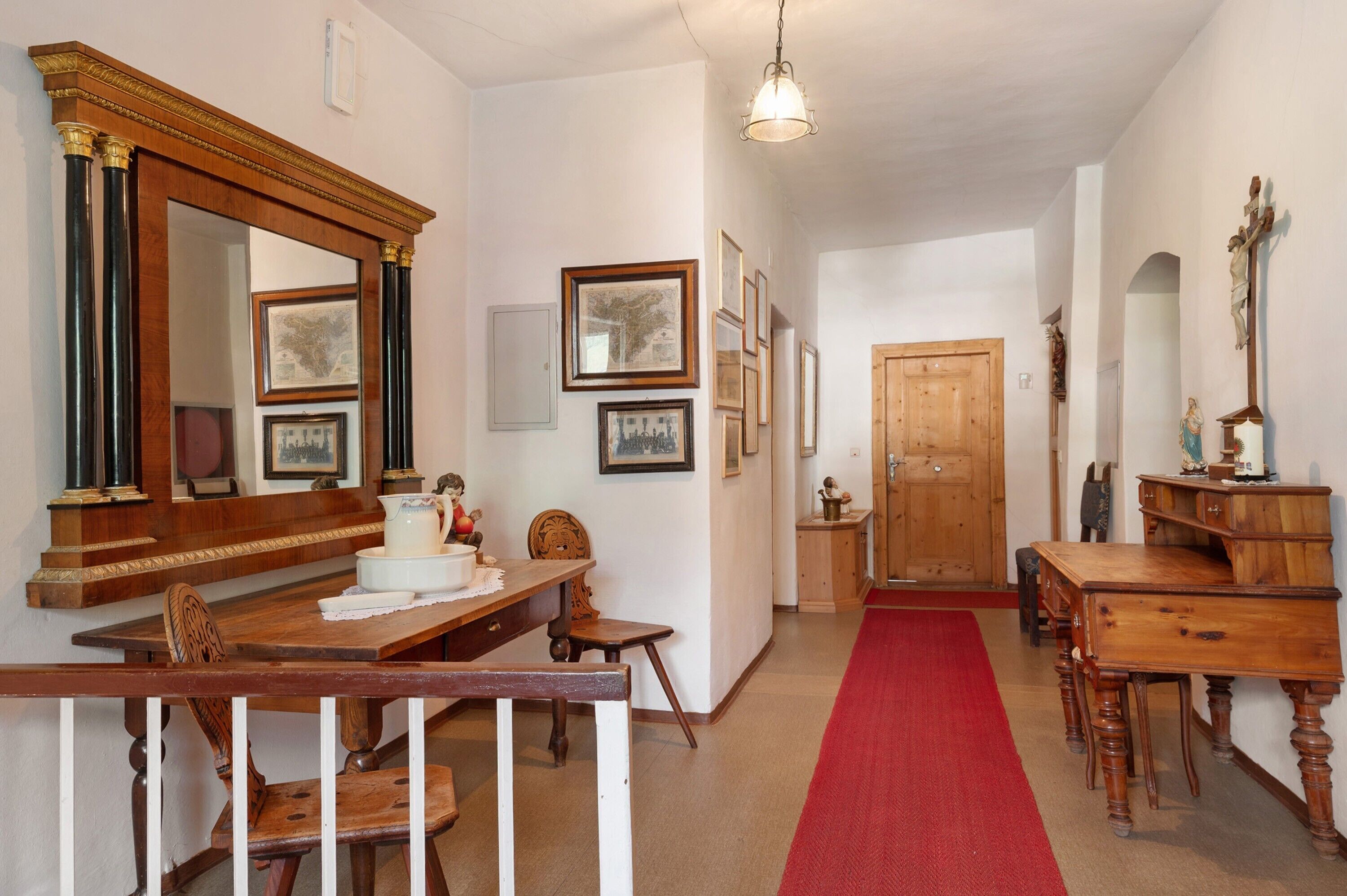A hallway with a wooden table, chairs, a red carpet, and framed pictures on the walls.
