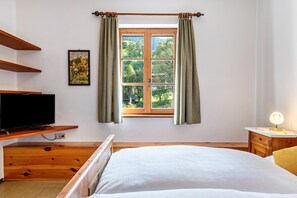 Une chambre à coucher avec un lit, une télévision, une fenêtre avec des rideaux, un tableau et une lampe de chevet.