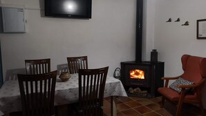 Un comedor con una mesa, sillas, un televisor montado en la pared, un estufa de leña y una silla roja.