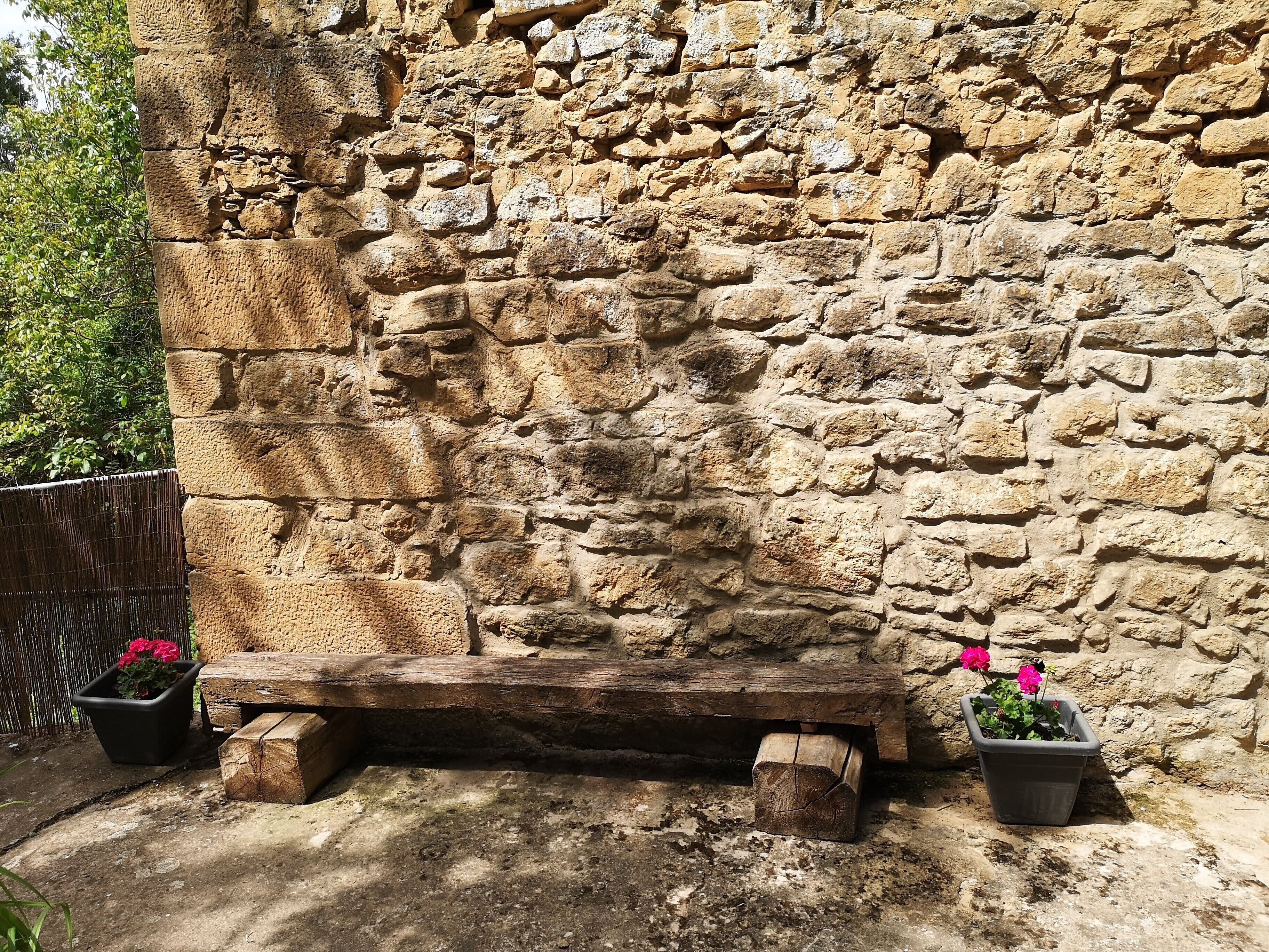 Un mur de pierre avec un banc en bois et des plantes en pot.