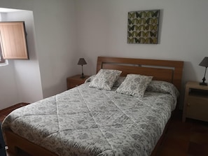 A neatly made bed with patterned bedding, two bedside tables with lamps, a wall-mounted artwork, and a wooden headboard.