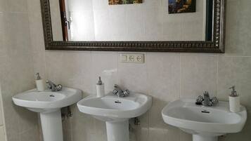 Un baño con tres lavamanos blancos, un espejo y dos cuadros colgados en la pared.