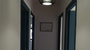 Un pasillo con suelo de baldosas, un colgador de luces y un aviso enmarcado en la pared.