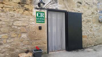 Un mur de pierres rustiques surmonté d’un portail en métal, une enseigne verte indiquant « CR CASA RURAL LANDETXEA », et une petite plante en pot.