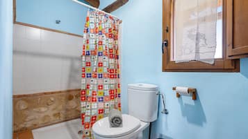 A bathroom with a toilet, a shower curtain, a window with a lace curtain, and a tiled wall.