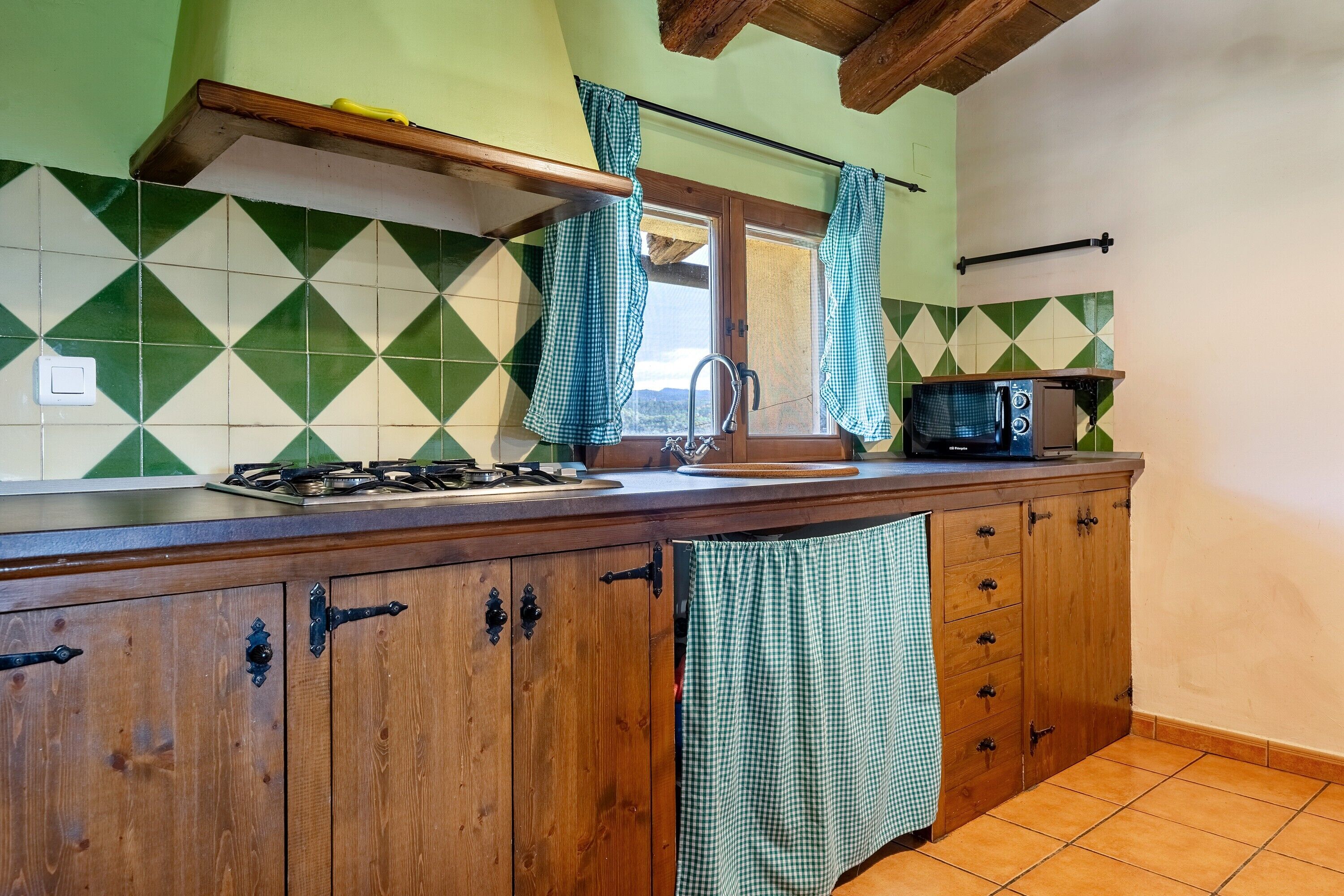 A kitchen with a gas stove, a microwave, and a window with curtains.
