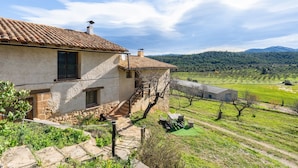 A rustic stone house with a tiled roof, a staircase leading to a balcony, and a vineyard in the background. - Country House 'La Sala' with Mountain View, Shared Pool and Wi-Fi (Peñarroya De Tastavins)