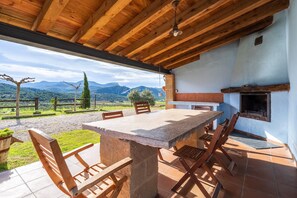 Un espacio de comedor al aire libre con una mesa de piedra y sillas de madera, una chimenea y vistas a las montañas.