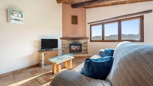 A living room with a fireplace, a television, and a large window. - Country House 'La Sala' with Mountain View, Shared Pool and Wi-Fi (Peñarroya De Tastavins)