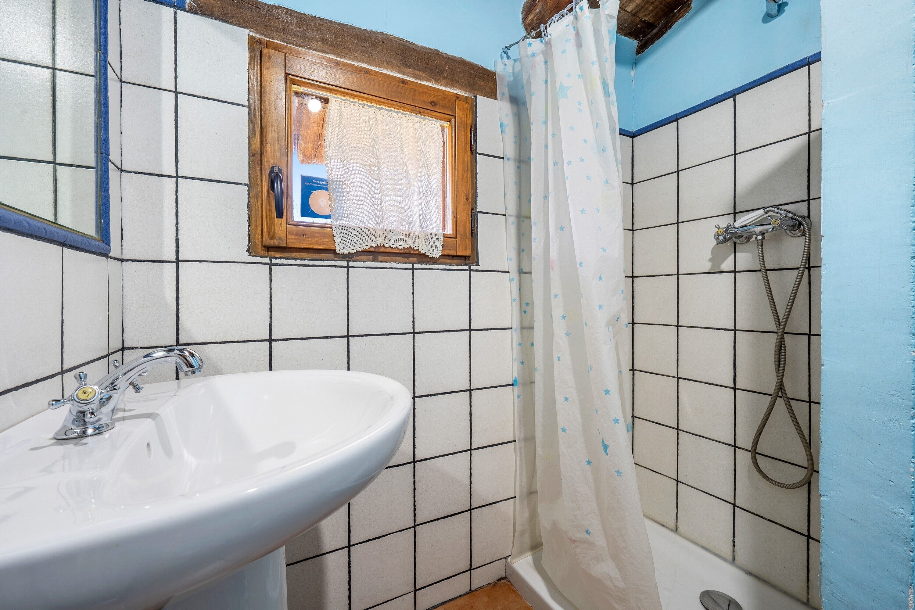 A bathroom with a white sink, a shower with a curtain, and a window with a towel.