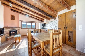 Un coin repas rustique avec une table et des chaises en bois, une cheminée et une vue sur les montagnes par la fenêtre.