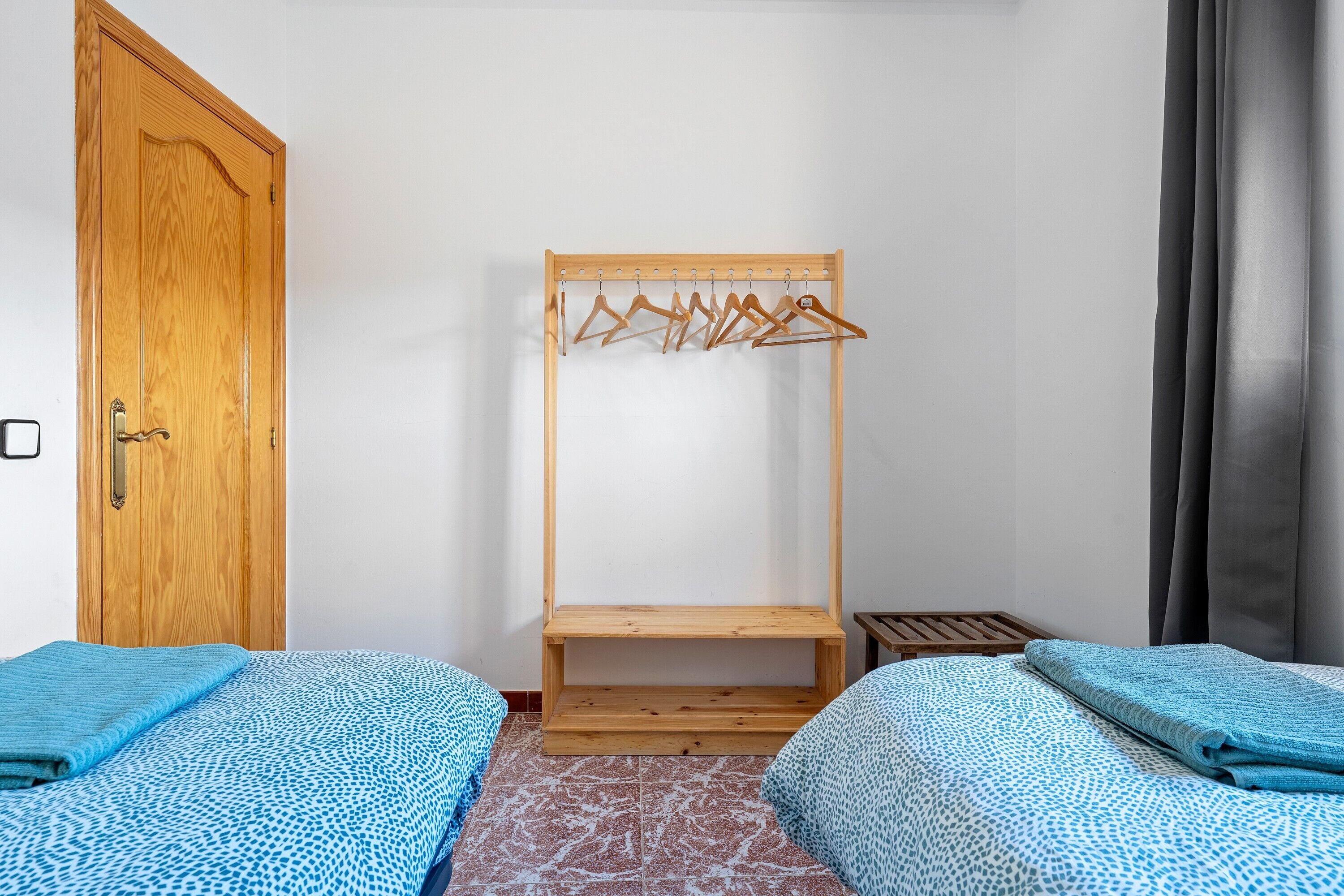 A room with two beds, a wooden wardrobe, a wooden drying rack, and a small wooden table.