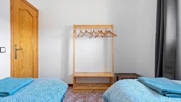 A room with two beds, a wooden wardrobe, a wooden drying rack, and a small wooden table.