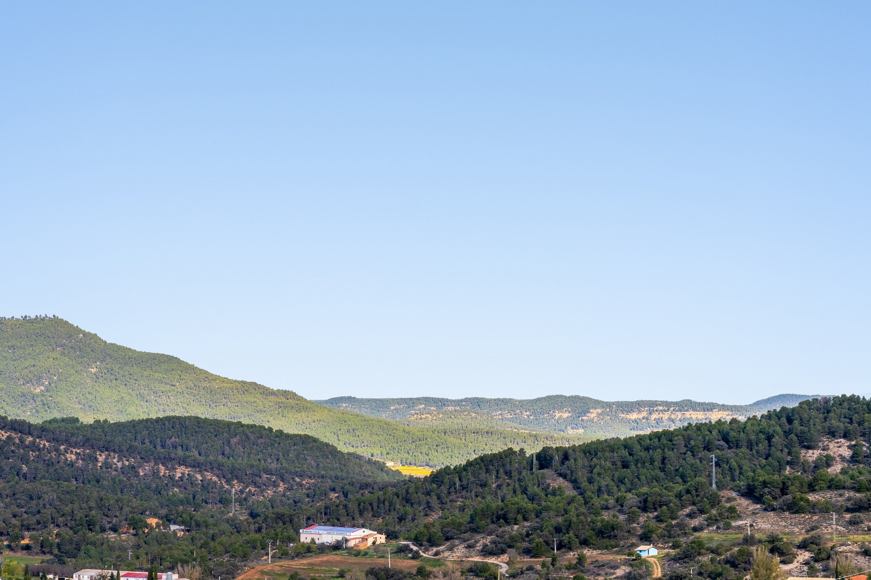 Un paisaje montañoso con algunos edificios, entre ellos un edificio blanco destacado con tejado rojo.