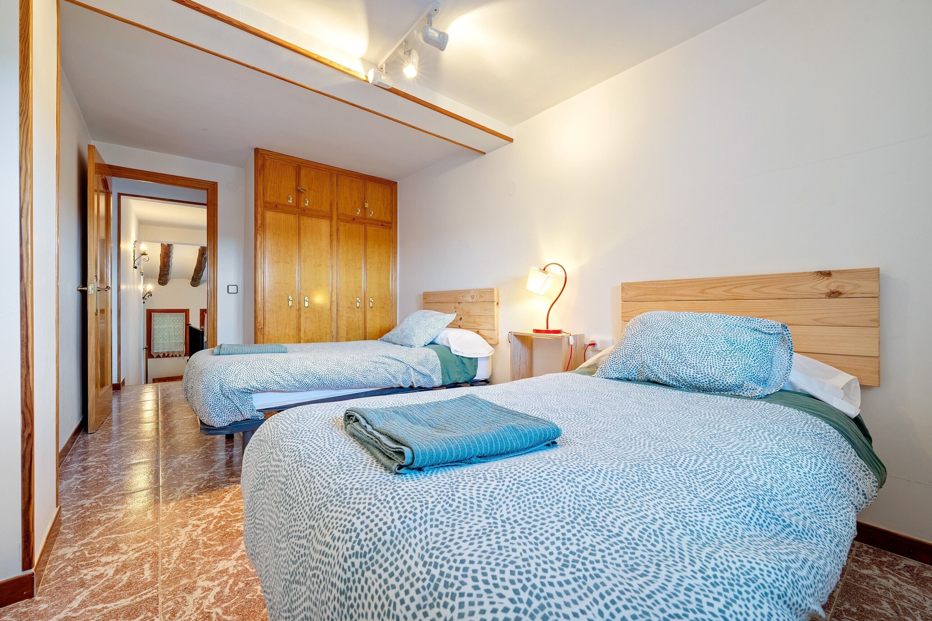 Une chambre d’hôtel avec deux lits, une armoire en bois, une table de chevet avec une lampe, et une salle de bain visible au fond.