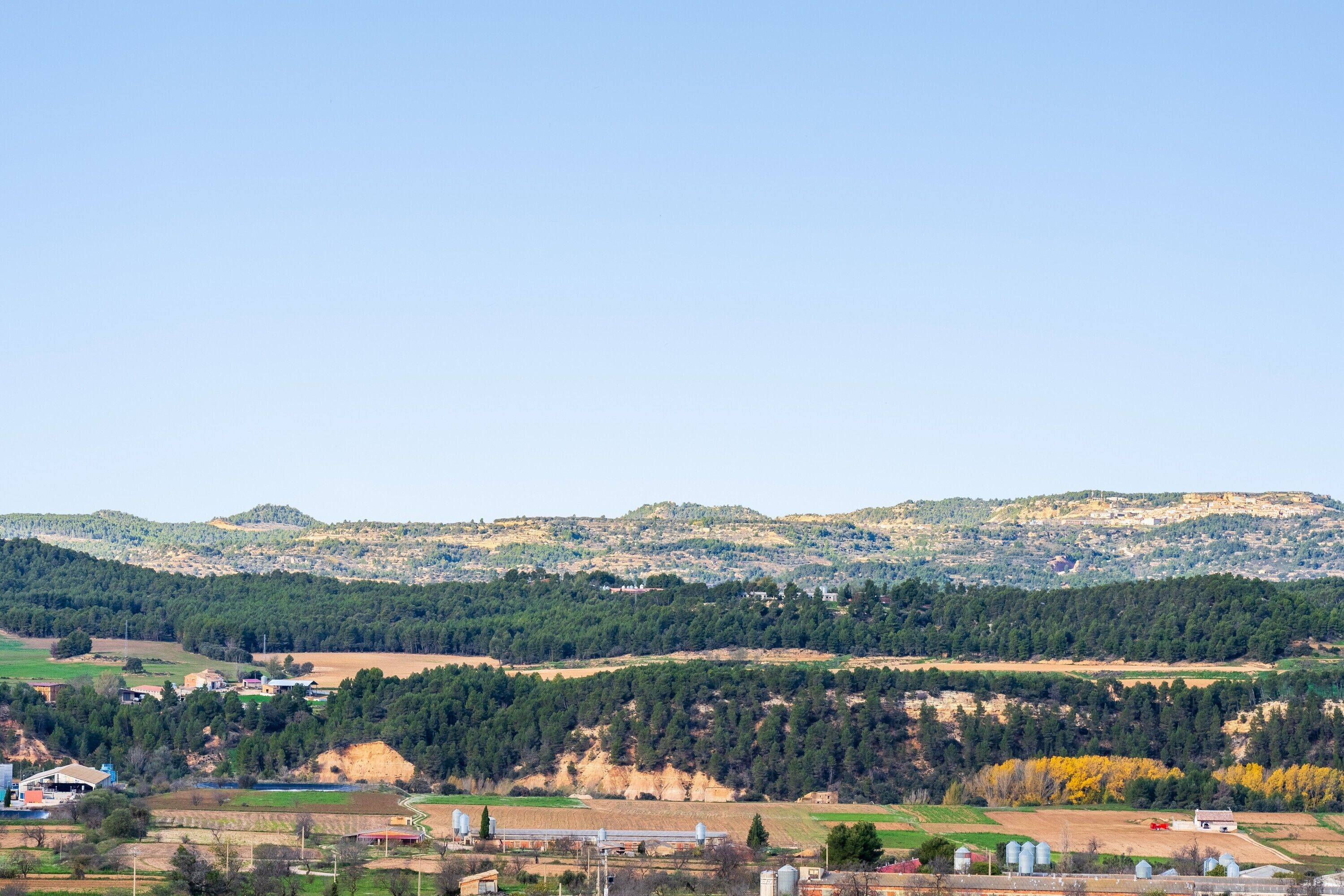Paisaje rural con cielo despejado, colinas onduladas y edificios dispersos.