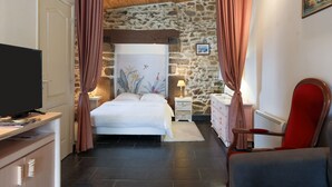 Un dormitorio con cama, televisor, cómoda, silla y pared de piedra.