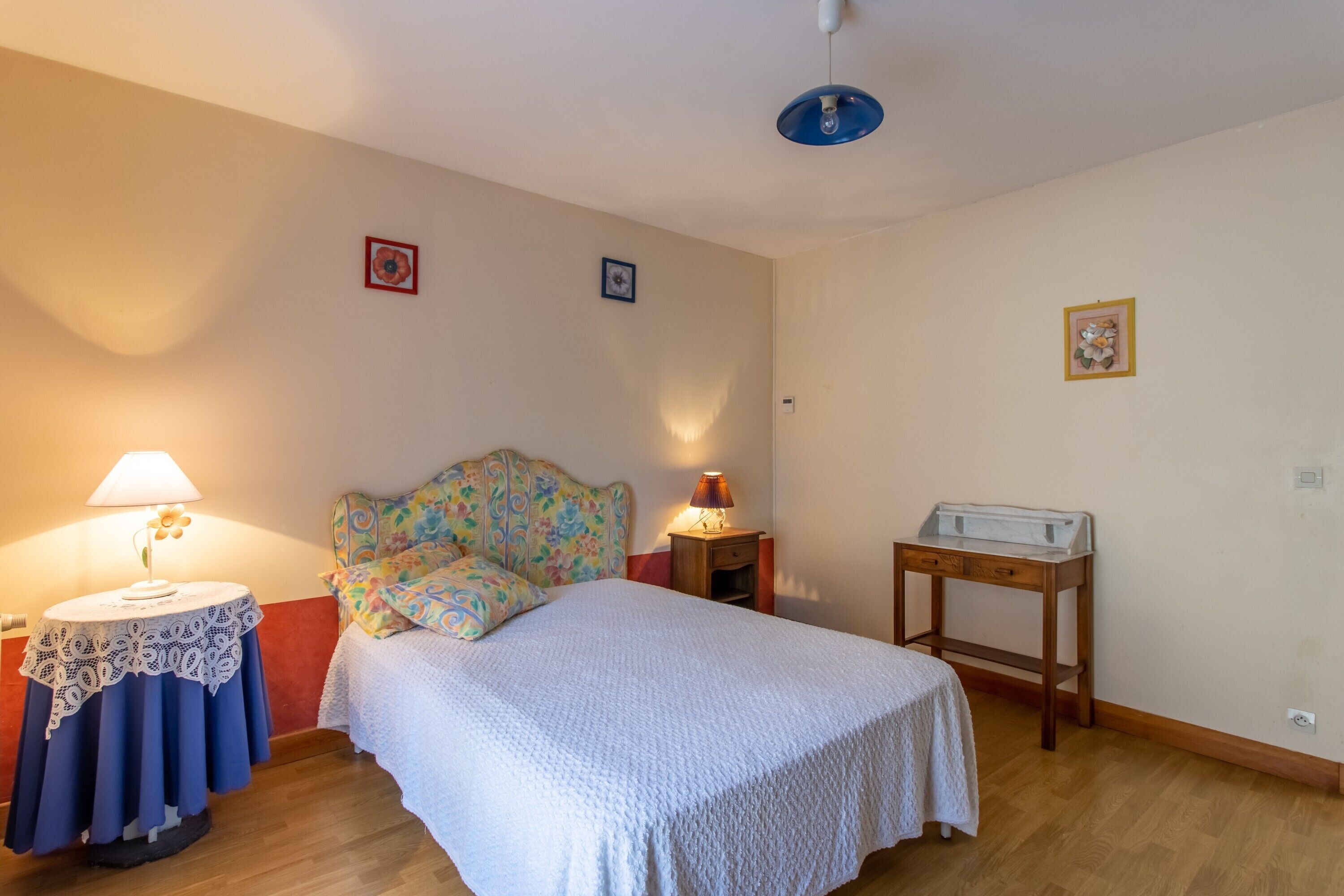 A bedroom with a bed, two bedside tables with lamps, a wooden nightstand, and a small table with a tray.