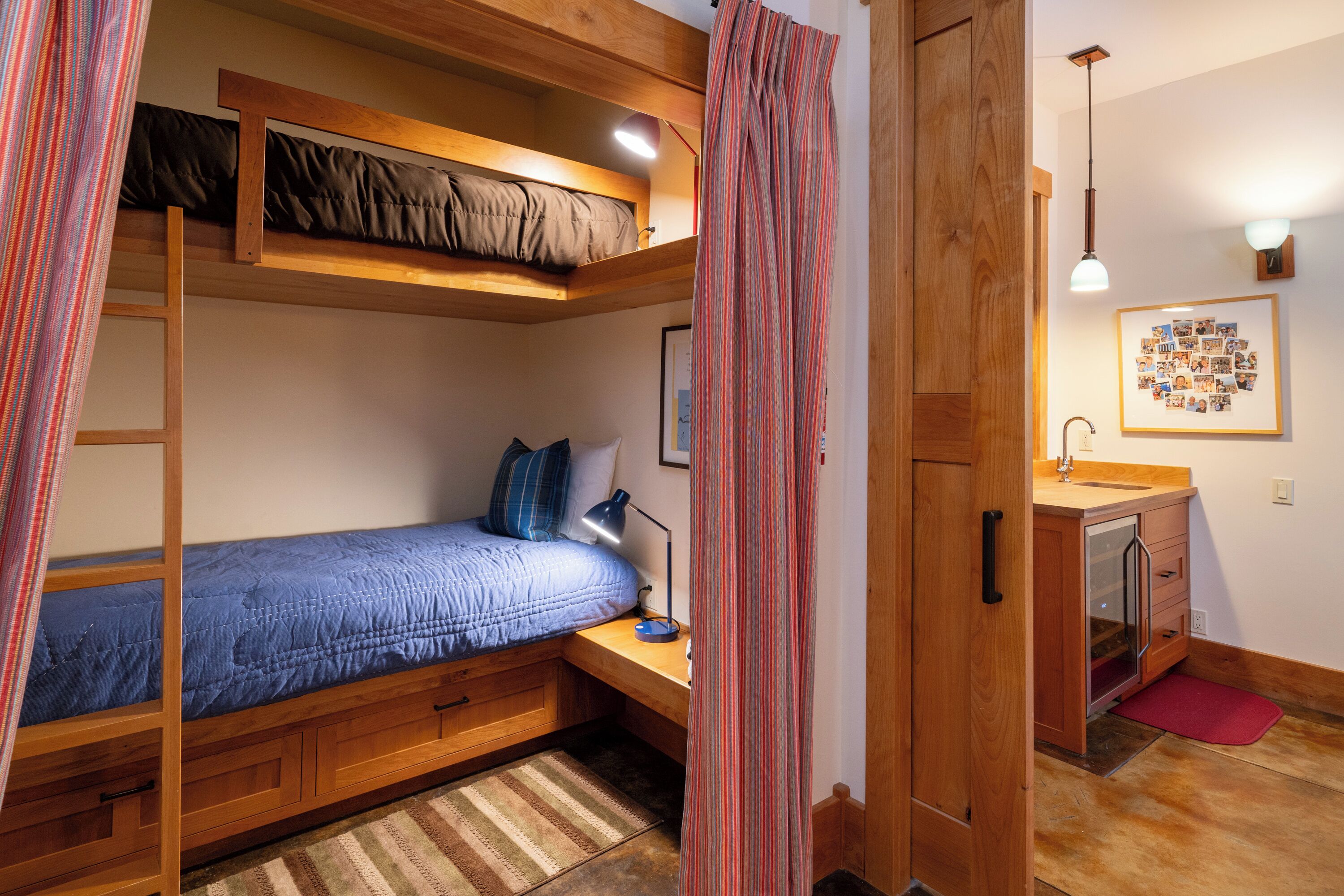 A compact bedroom with a bunk bed, a desk with a lamp, a small bathroom, and a wooden cabinet.