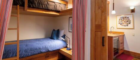 A compact bedroom with a bunk bed, a desk with a lamp, a small bathroom, and a wooden cabinet.