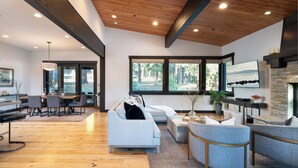 A spacious living area with a wooden ceiling, large windows, a fireplace, and modern furniture.